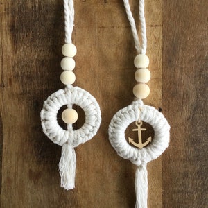 Peut inclure: Deux suspensions murales en macramé blanc avec des perles en bois et des glands. L'une a un charme d'ancre en bois.