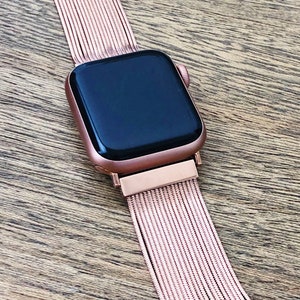 May include: A rose gold Apple Watch with a rose gold metal band. The band is made of a series of thin, interwoven metal strands.