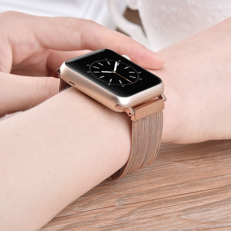 May include: A gold-toned Apple Watch with a rose gold metal band. The watch face is black with white hands and numbers.