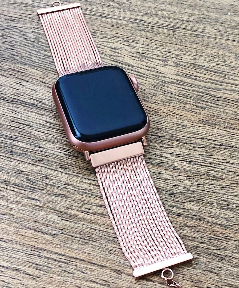 May include: A rose gold Apple Watch with a rose gold metal band. The band is made of a series of thin, interwoven metal strands.