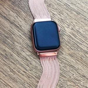 May include: A rose gold Apple Watch with a rose gold metal band. The band is made of a series of thin, linked metal strips.