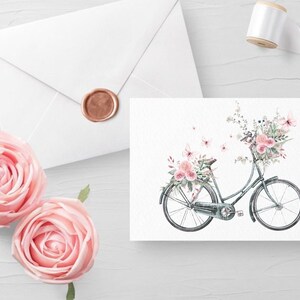 Pu&ograve; includere: Un'illustrazione ad acquerello di una bicicletta vintage con un cestino pieno di fiori rosa. La bicicletta &egrave; dipinta di blu chiaro e ha uno sfondo bianco.