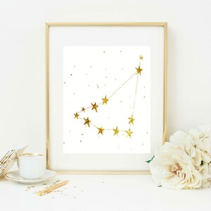 May include: A gold glitter constellation print in a gold frame. The constellation is of Capricorn, with a white background.