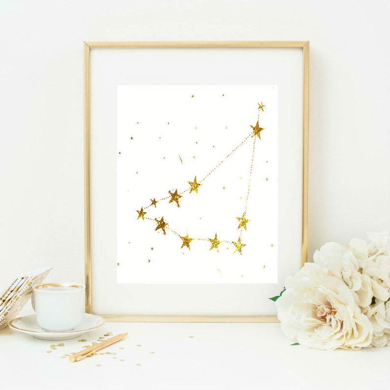 May include: A gold glitter constellation print in a gold frame. The constellation is of Capricorn, with a white background.