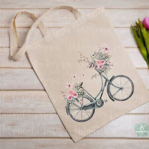 Pu&ograve; includere: Una borsa di tela bianca con un design floreale e una bicicletta vintage con un cestino pieno di fiori. La bicicletta &egrave; blu e ha una sella marrone. I fiori sono rosa e bianchi.