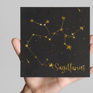 May include: A black card with gold glitter outlining the constellation Sagittarius. The text "Sagittarius" is written in gold glitter below the constellation.