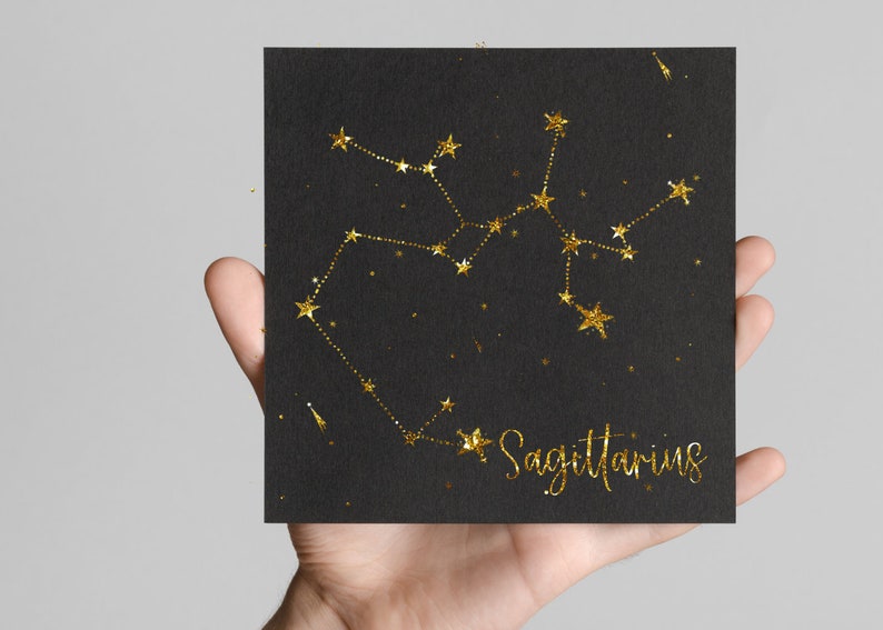 May include: A black card with gold glitter outlining the constellation Sagittarius. The text "Sagittarius" is written in gold glitter below the constellation.