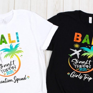May include: Two t-shirts with a graphic design of a palm tree, airplane, and the text "Bali Straight Trippin 2025". One shirt is white with the text "Vacation Squad" and the other is black with the text "Girls Trip".