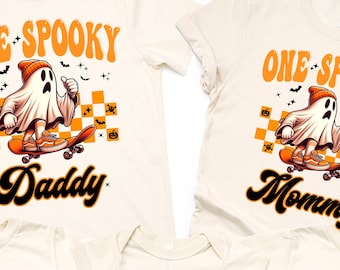 May include: A collection of off-white Halloween-themed t-shirts and a onesie. Each shirt features a cartoon ghost on a skateboard with the text "ONE SPOOKY" and a family member's title: "Daddy", "Mommy", "Dude", "Sister", and "Brother".