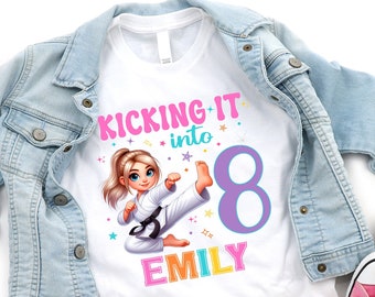 May include: White t-shirt with a pink, blue, and yellow graphic of a girl in a karate pose. The text "Kicking it into 8" and "EMILY" are on the shirt.