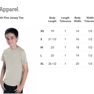 Peut inclure: Un jeune portant un t-shirt beige &agrave; col rond. L'image comprend un tableau des tailles avec des mesures en centim&egrave;tres pour la longueur du corps, la largeur et la longueur des manches. Le t-shirt est de LAT Apparel, style 6101 Youth Fine Jersey Tee.