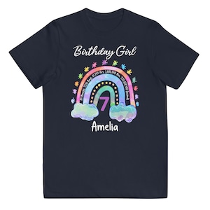 May include: Navy blue t-shirt with a rainbow design and the text "Birthday Girl". The rainbow has a number 7 in the center and the text "84 Months, 2556 Days 61,344 Hrs. 3,680,640 Min 220,838,400 Seconds" around it. The name "Amelia" is written below the rainbow.