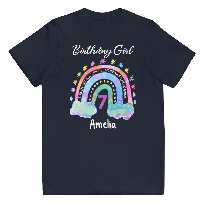 May include: Navy blue t-shirt with a rainbow design and the text "Birthday Girl". The rainbow has a number 7 in the center and the text "84 Months, 2556 Days 61,344 Hrs. 3,680,640 Min 220,838,400 Seconds" around it. The name "Amelia" is written below the rainbow.