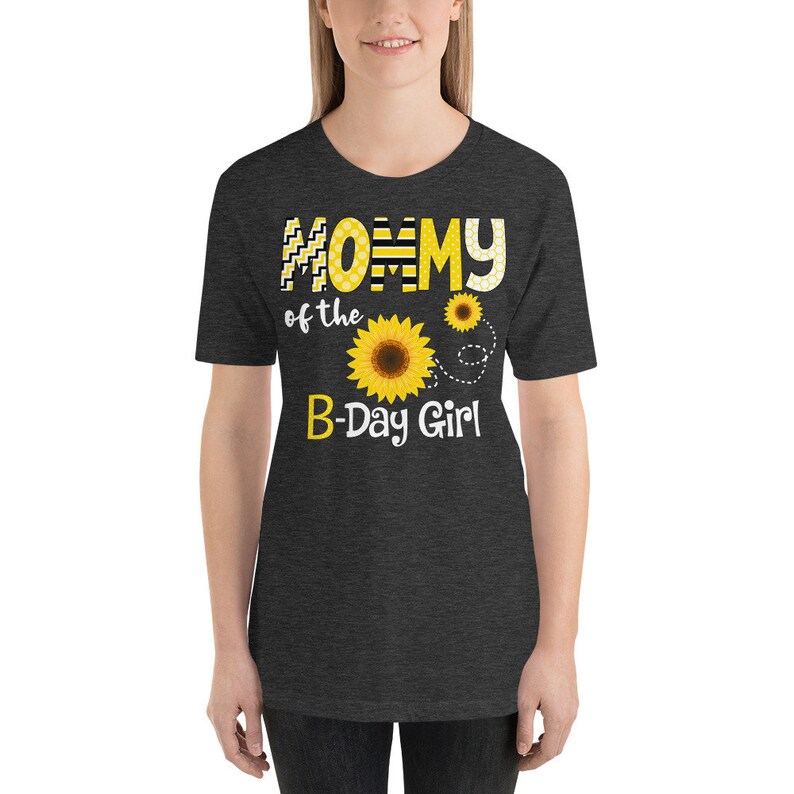 Peut inclure: T-shirt gris fonc&eacute; avec l'inscription "Mommy of the B-Day Girl" en jaune et blanc. Le motif comprend un tournesol et deux petits tournesols. Le t-shirt &agrave; manches courtes a un col rond.