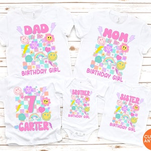 May include: White t-shirts with vibrant graphics for a birthday. The designs feature text such as "DAD", "MOM", "BROTHER", and "SISTER", alongside smiley faces, rainbows, and lightning bolts. The shirts are for the "BIRTHDAY GIRL".