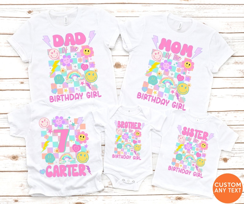 May include: White t-shirts with vibrant graphics for a birthday. The designs feature text such as "DAD", "MOM", "BROTHER", and "SISTER", alongside smiley faces, rainbows, and lightning bolts. The shirts are for the "BIRTHDAY GIRL".