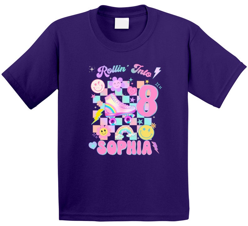 以下が含まれることがあります： 紫色のTシャツに、ピンクとブルーのローラースケートのグラフィック、虹、そして「Rollin' Into 8 Sophia」の文字がプリントされています。