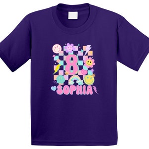 May include: A purple t-shirt with a vibrant design for an eighth birthday celebration. The design incorporates a checkered pattern, the number 8, the name Sophia, and cheerful smiley faces, flowers, and lightning bolts.