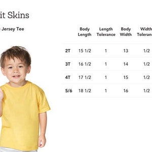 Peut inclure: Un enfant portant un t-shirt jaune. L'image comprend le texte "Rabbit Skins" et "3321 Fine Jersey Tee". Un tableau affiche les mesures pour diff&eacute;rentes tailles, notamment la longueur du corps, la largeur et la longueur des manches, en centim&egrave;tres.
