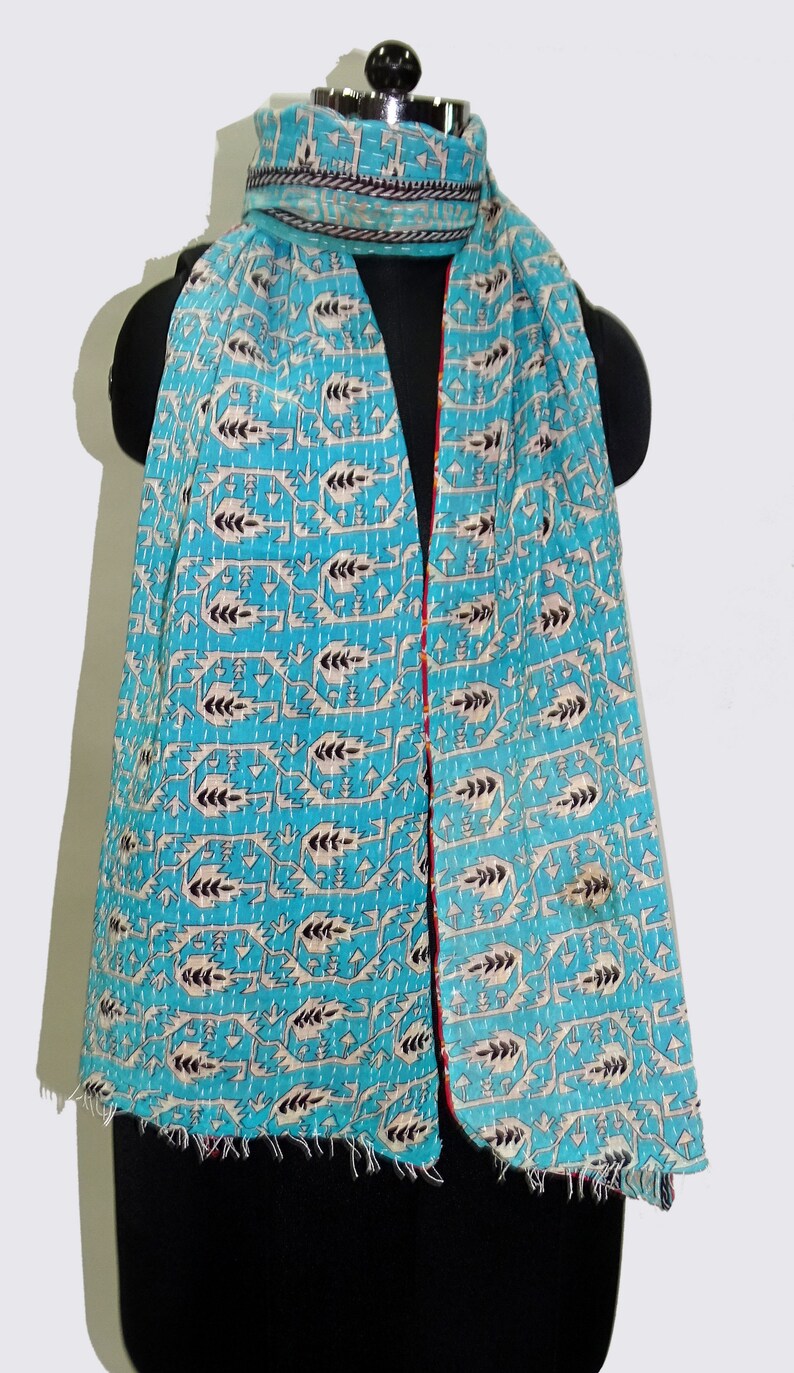 May include: A turquoise blue kantha scarf with a white and black geometric pattern. The scarf has a red and white trim and a frayed edge.