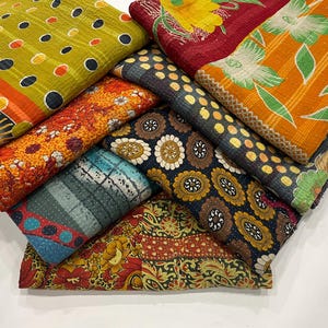 Pode incluir: Uma pilha de pe&ccedil;as de tecido coloridas e estampadas. Os tecidos apresentam v&aacute;rios desenhos, incluindo bolinhas, estampas florais e formas geom&eacute;tricas. As cores incluem amarelo, laranja, vermelho, azul e preto. Os tecidos parecem estar dobrados e empilhados juntos.