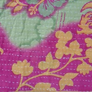 Pode incluir: Close-up de um tecido vibrante com um design floral. O tecido apresenta uma combina&ccedil;&atilde;o de rosa, verde e dourado. O design inclui grandes padr&otilde;es florais e formas menores em forma de folha, todos costurados com fio branco.