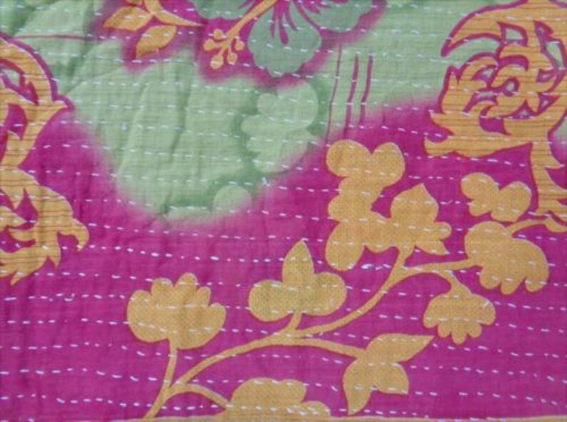 Pode incluir: Close-up de um tecido vibrante com um design floral. O tecido apresenta uma combina&ccedil;&atilde;o de rosa, verde e dourado. O design inclui grandes padr&otilde;es florais e formas menores em forma de folha, todos costurados com fio branco.