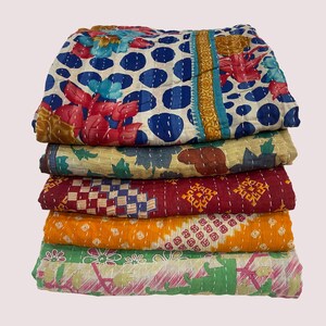Pode incluir: Uma pilha de cinco colchas coloridas e estampadas. A colcha superior apresenta um fundo branco com bolinhas azuis e desenhos florais em vermelho e turquesa. Outras colchas exibem v&aacute;rios padr&otilde;es em tons de vermelho, laranja, verde e amarelo.