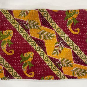 Pode incluir: T&ecirc;xtil dobrado com um padr&atilde;o repetido de cavalos-marinhos e motivos de folhas. O fundo &eacute; vermelho escuro, com detalhes diagonais amarelos e verdes. As bordas s&atilde;o adornadas com uma borda decorativa.