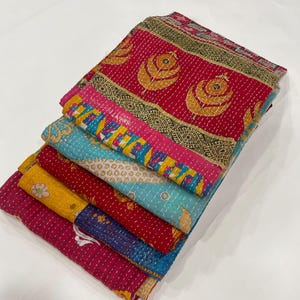 Pode incluir: Uma pilha de pe&ccedil;as de tecido bordado coloridas. Os t&ecirc;xteis apresentam uma variedade de padr&otilde;es e cores, incluindo vermelho, amarelo, azul e rosa. As pe&ccedil;as s&atilde;o dobradas e empilhadas, mostrando os intrincados detalhes de costura e design.