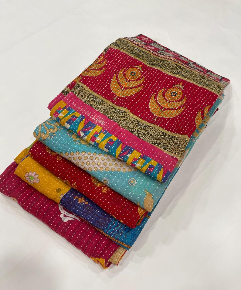 Pode incluir: Uma pilha de pe&ccedil;as de tecido bordado coloridas. Os t&ecirc;xteis apresentam uma variedade de padr&otilde;es e cores, incluindo vermelho, amarelo, azul e rosa. As pe&ccedil;as s&atilde;o dobradas e empilhadas, mostrando os intrincados detalhes de costura e design.