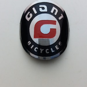 以下が含まれることがあります： 赤と白の文字「G」を囲む円の中に「GIANT」という文字が書かれた、黒と銀の自転車のロゴ。円の真下に「BICYCLES」という文字が書かれている。