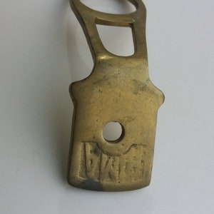May include: A brass keyhole cover with a rounded rectangular shape and a hole in the center. The cover has the word "GENOA" embossed on the bottom.