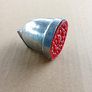 May include: A silver stamp with a red patterned base. The stamp has a rounded top and a flat, circular base with a detailed design. The stamp is likely used for decorative purposes or crafting.