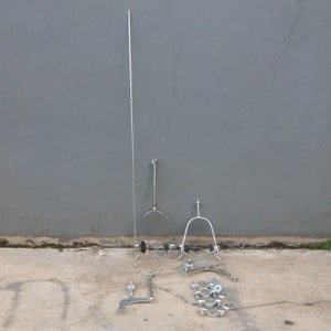 May include: A set of silver bicycle parts, including a long, thin rod, two curved metal pieces, and several smaller metal pieces. The parts are arranged on a concrete surface.