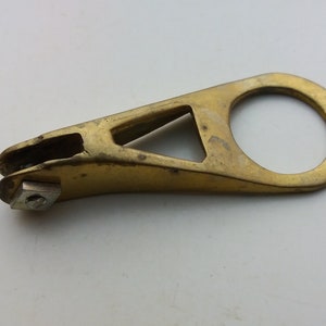 May include: A gold-colored metal bike chain tool with a small, round hole at one end and a small, square-shaped piece of metal at the other end.