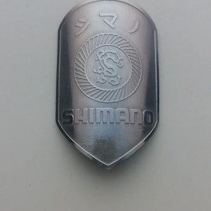 May include: A silver Shimano bicycle part with the word "Shimano" and Japanese characters printed on it.