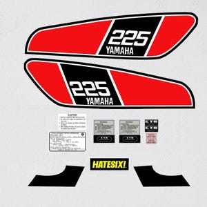 Puede incluir: Un conjunto de calcomanías para motocicletas Yamaha 225 en rojo, negro y blanco. Las calcomanías incluyen el número "225" y el logotipo de Yamaha. También se incluyen pegatinas más pequeñas con advertencias y el texto "HATESIX!".