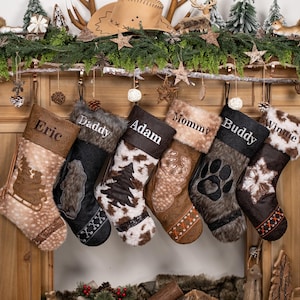 May include: Six personalized Christmas stockings hang from a wooden mantel. Each stocking features a different design, including a tree, paw print, and snowflake, with names like "Eric" and "Mommy" embroidered on them. The stockings have faux fur trim.