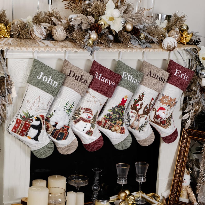 Puede incluir: Siete calcetines navide&ntilde;os cuelgan sobre una chimenea. Cada calcet&iacute;n tiene un nombre bordado en el pu&ntilde;o. Los calcetines presentan dise&ntilde;os festivos como un ping&uuml;ino, un mu&ntilde;eco de nieve y Pap&aacute; Noel, con detalles en verde, rojo y beige.