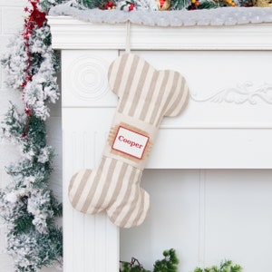 May include: A beige and white striped dog bone-shaped Christmas stocking with a burlap tag that says "Cooper" in red lettering.