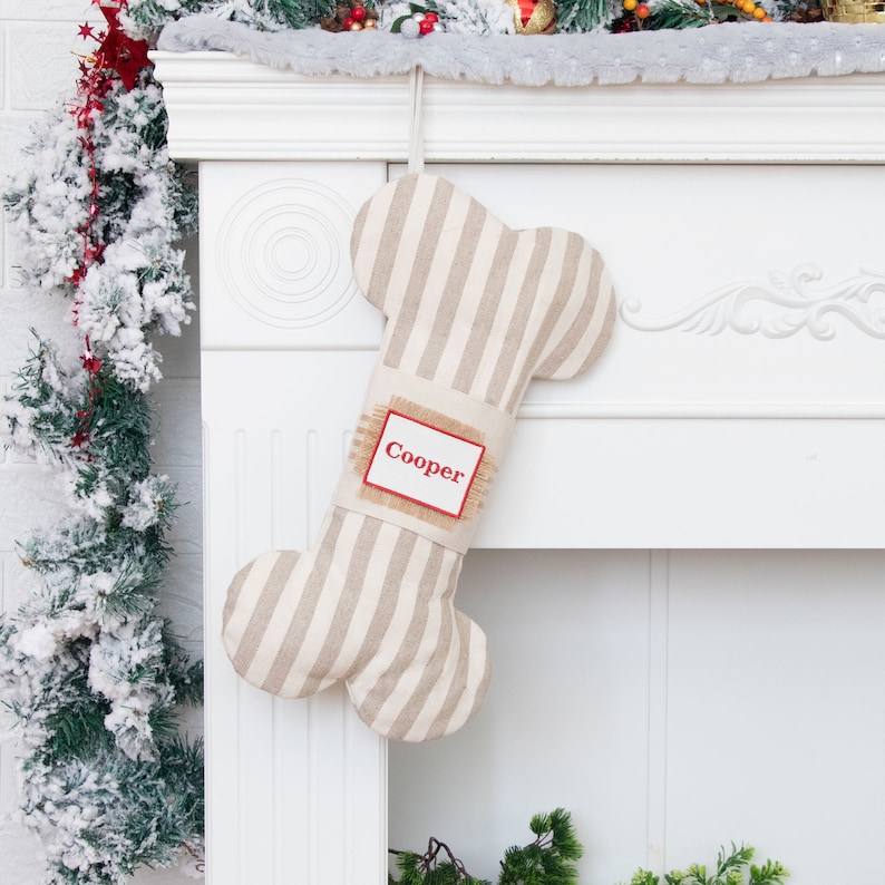 May include: A beige and white striped dog bone-shaped Christmas stocking with a burlap tag that says "Cooper" in red lettering.