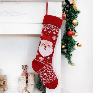 May include: Red Christmas stocking with a Santa Claus face and snowflake pattern. The stocking is hanging on a white mantelpiece. A festive decoration for the holiday season.