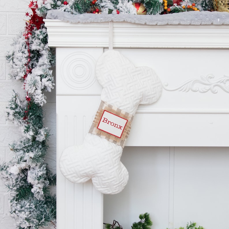 May include: White bone-shaped Christmas stocking with a burlap tag that says "Bronx" in red lettering. The stocking is hanging on a white fireplace mantel.