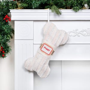May include: White plush dog bone stocking with a red and white personalized tag that says "Poppy".