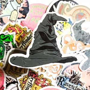 Pode incluir: Um adesivo preto e branco do Chapéu Seletor da série Harry Potter. O chapéu está sobre um fundo de outros adesivos, incluindo os brasões das casas de Hogwarts.