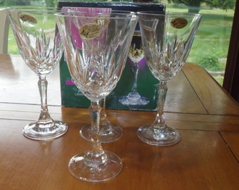 May include: Four clear glass wine glasses with a cut crystal design. The glasses are on a wooden table.