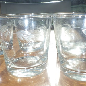 Op de afbeelding: Set van zes heldere glazen tumblers met een gegraveerd tarwemotief. De glazen zijn leeg en staan op een houten oppervlak.
