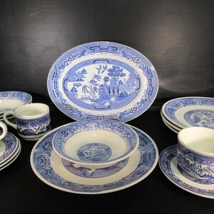 Op de afbeelding: Een set blauw en wit porselein met een wilgenmotief, inclusief een grote ovale serveerschaal, dinerborden, een soepkom, theekopjes en schoteltjes.