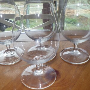 Puede incluir: Tres copas de brandy de vidrio transparente sobre una mesa de madera. Las copas están vacías y tienen una copa redonda y un tallo corto.